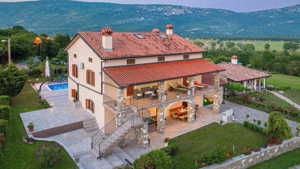 A two-story house with a red-tiled roof, a swimming pool, and a stone staircase leading to a covered patio.