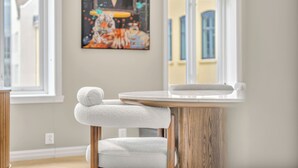 A room with a round wooden table, a white cushioned chair, and a painting on the wall.