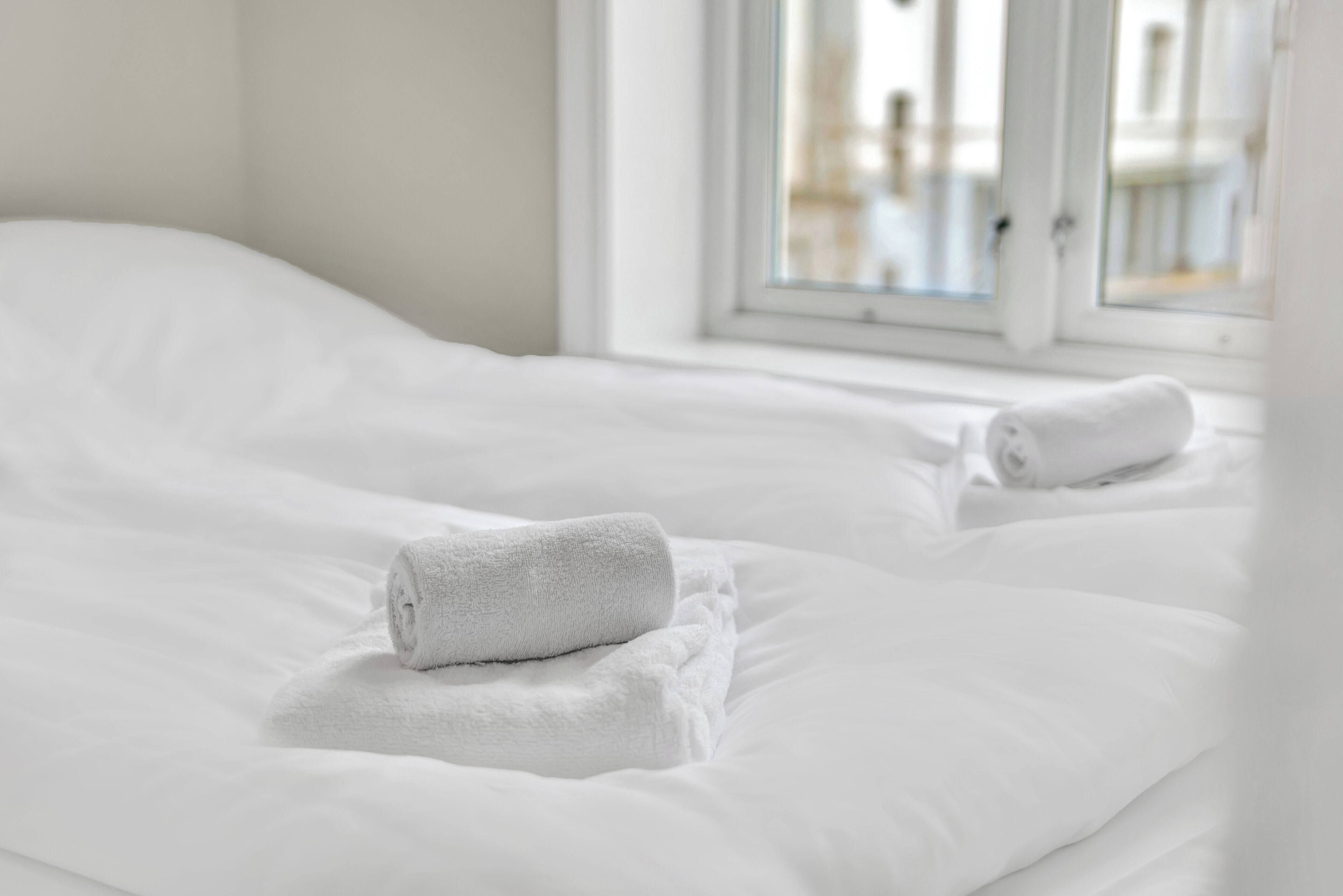 Een opgemaakt bed met witte lakens en twee opgerolde handdoeken.