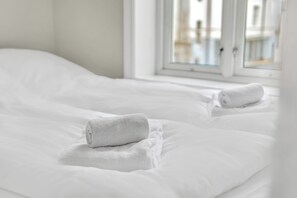 Een opgemaakt bed met witte lakens en twee opgerolde handdoeken.
