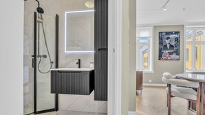 A modern bathroom with a glass-enclosed shower, a vanity with a mirror, and a dining area with a table and chairs.