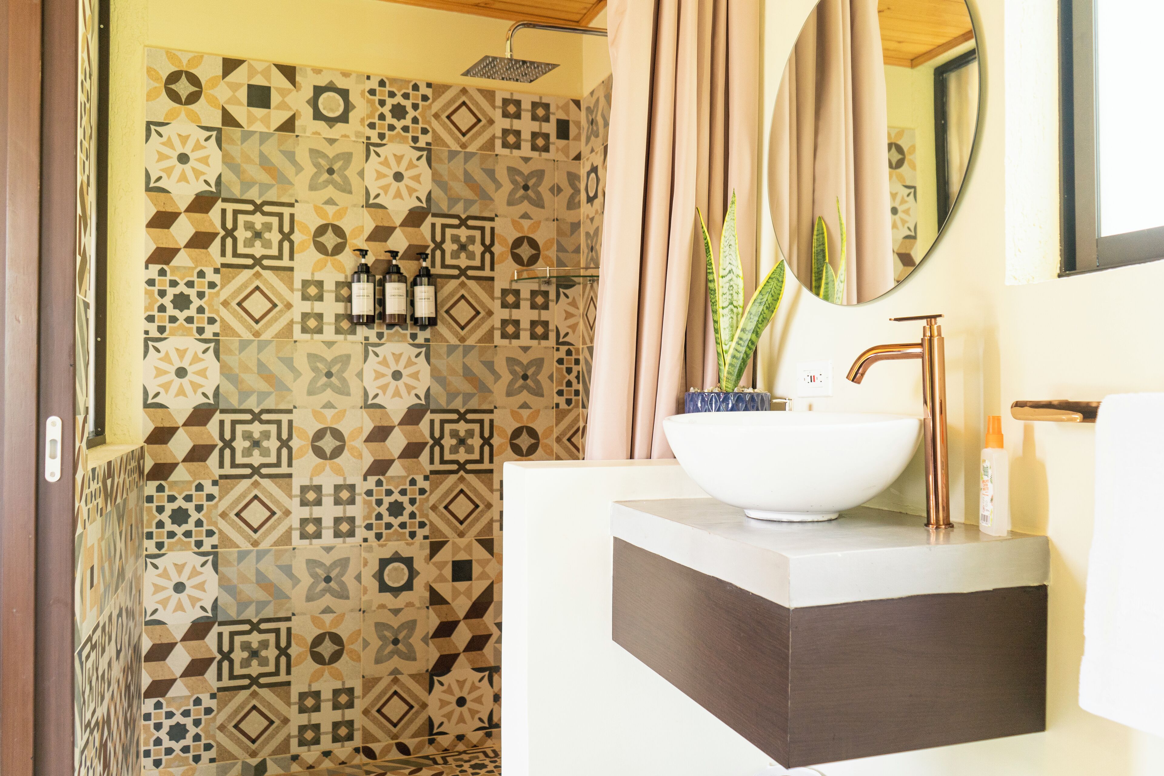 A bathroom with patterned tiles, a white sink, a mirror, and a shower area.