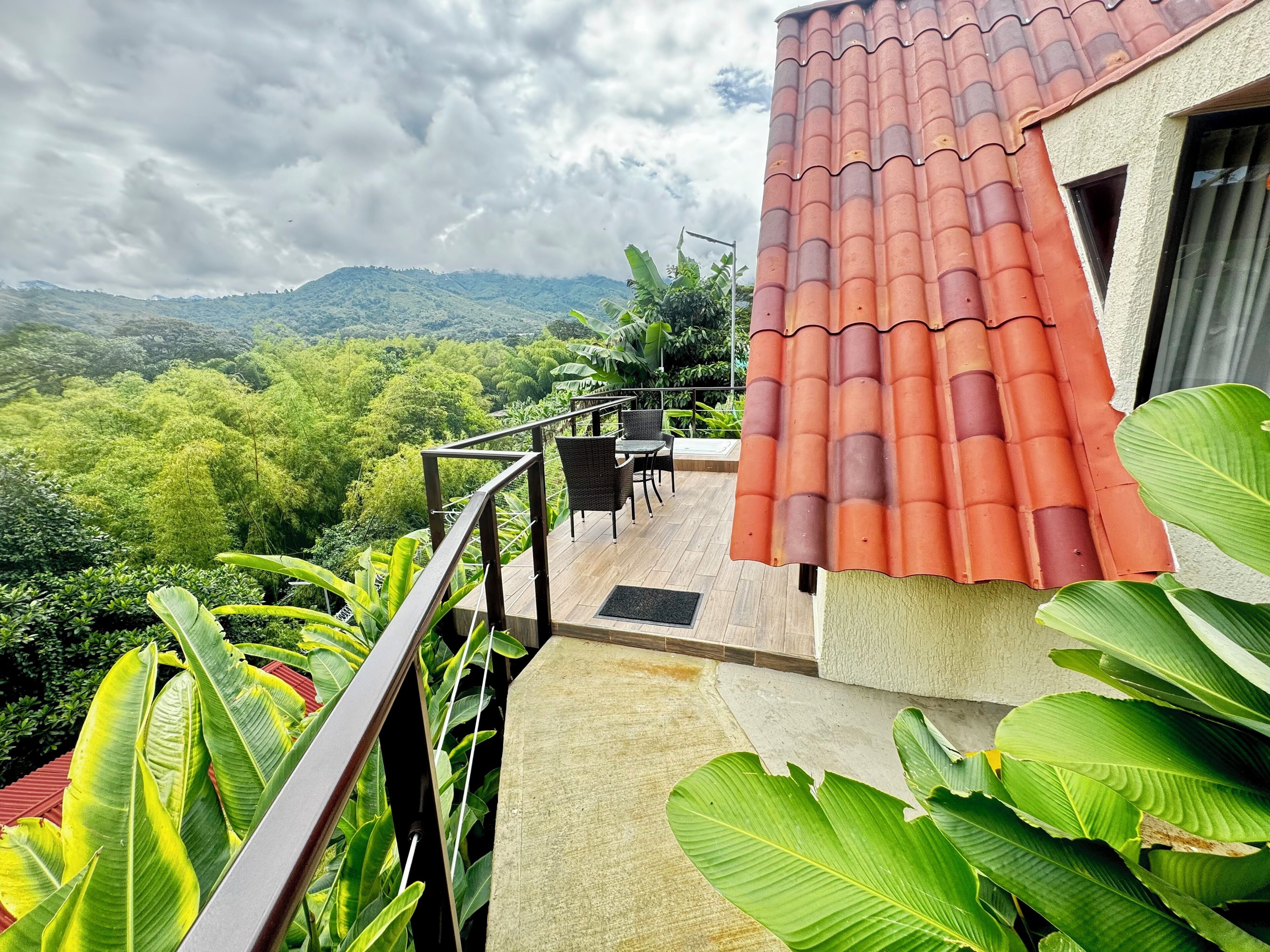 Terraço com telhado de telhas vermelhas, rodeado por vegetação exuberante e vista para colinas ao longe.