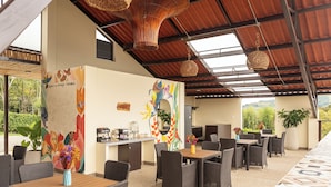 A covered outdoor dining area with wicker furniture and a mural on the wall. - Pachakuti Ecovida Hotel (Caicedonia)