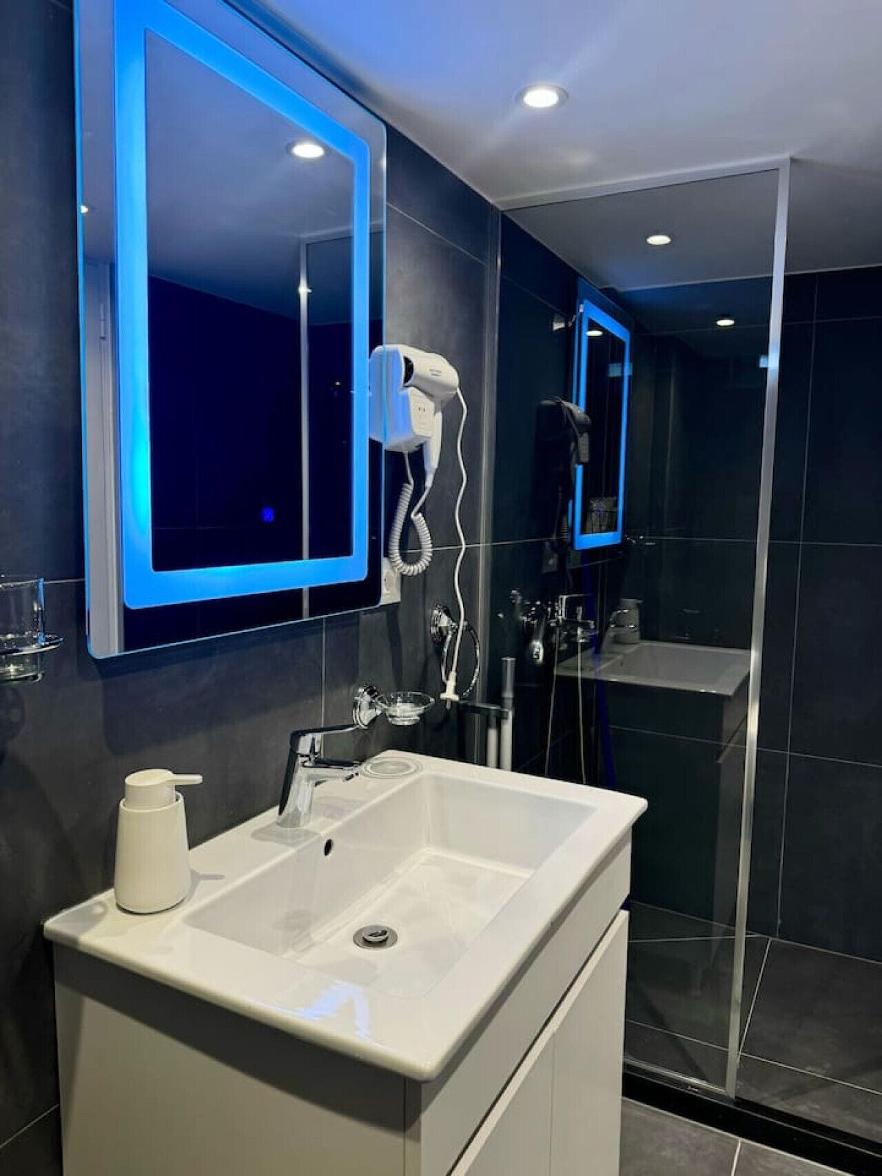 A modern bathroom with a large mirror, a white sink, and a hairdryer.