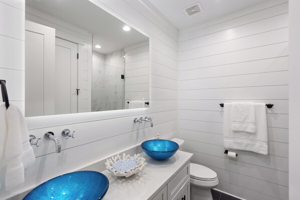 A modern bathroom with a white vanity, two sinks, a large mirror, and a toilet.