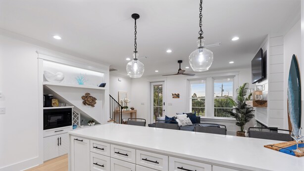 Una cocina moderna con armarios blancos, una isla grande, iluminación colgante y vistas al exterior.