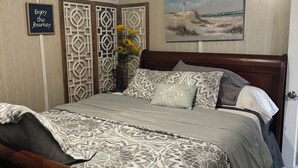 A bedroom with a bed, a painting of a beach scene, a decorative wall panel, and a sign that says "Enjoy the Journey."