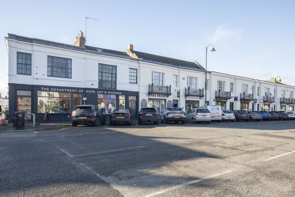 A row of white buildings with shops on the ground floor, including 'The Department of Hope, Joy & Wonder' and 'Woli Trading'.