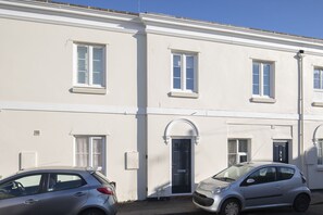 A row of white buildings with multiple windows and doors, parked cars, and a clear blue sky.