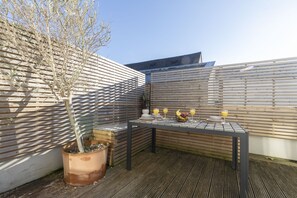 An outdoor patio with a table set for breakfast, a potted plant, and a wooden fence.