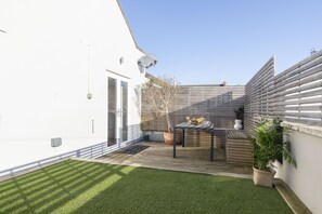 A modern outdoor patio with a wooden deck, a small table with chairs, and a potted plant.