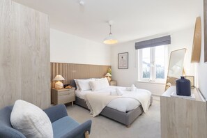 A modern bedroom with a bed, bedside tables, a chair, a dresser, and a window with a view.