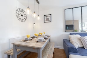A dining area with a wooden table set for four, a clock, pendant lights, and a framed picture on the wall.