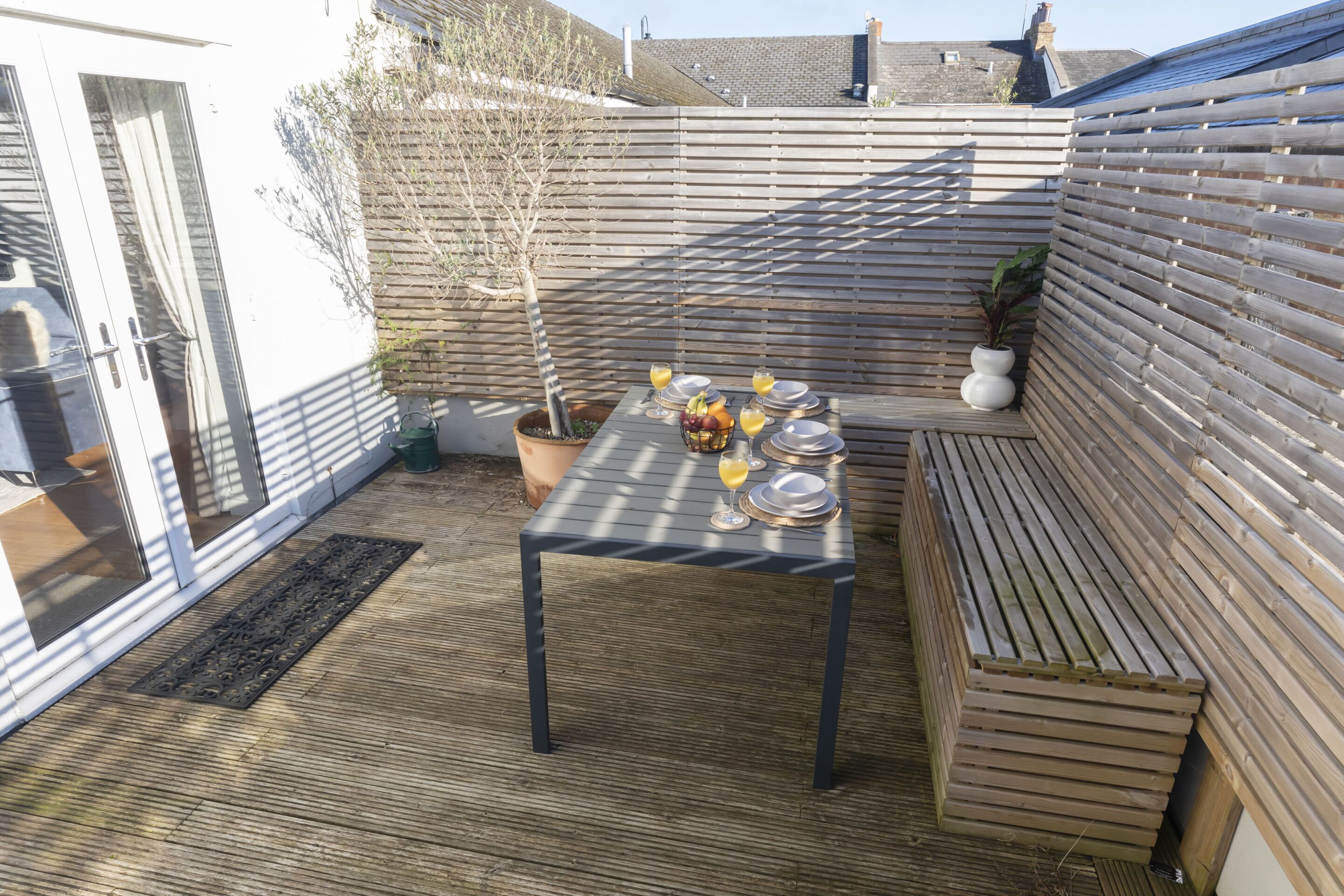 A wooden deck with a table set for a meal, surrounded by a wooden fence and a potted plant.