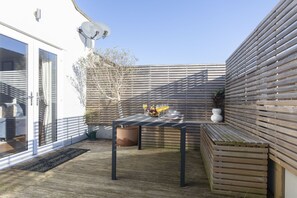 A patio with a table set for two, a wooden bench, and a potted plant.