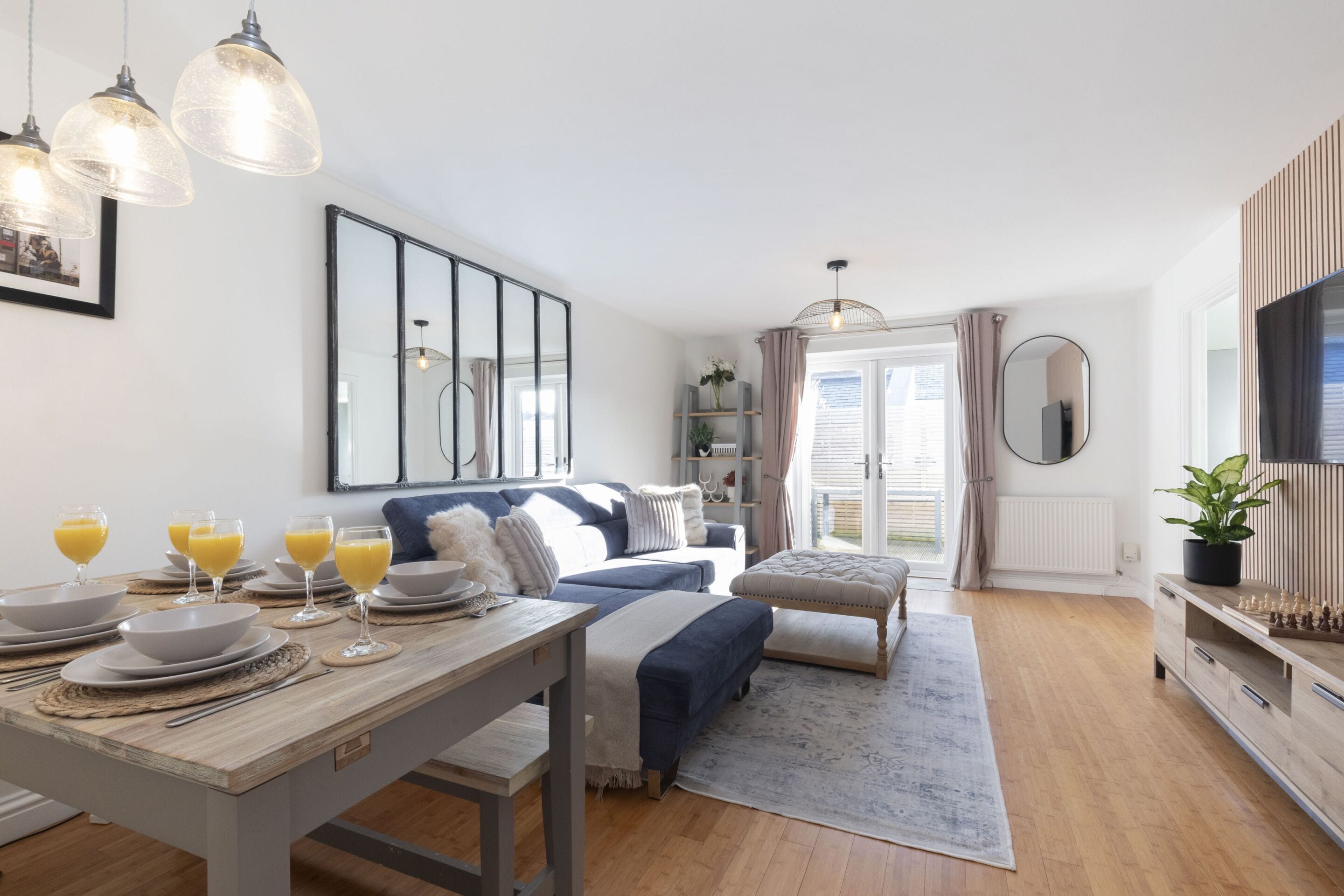 A modern bedroom with a bed, bedside tables, a desk with breakfast items, and a large window with curtains.
