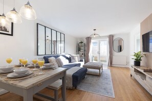 A modern bedroom with a bed, bedside tables, a desk with breakfast items, and a large window with curtains. - Cosy 2-Bed Apartment in Tivoli (Gloucestershire)