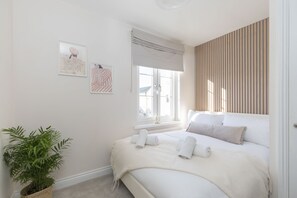 A bedroom with a large bed, a window with a view, a potted plant, and two framed artworks on the wall. - Cosy 2-Bed Apartment in Tivoli (Gloucestershire)