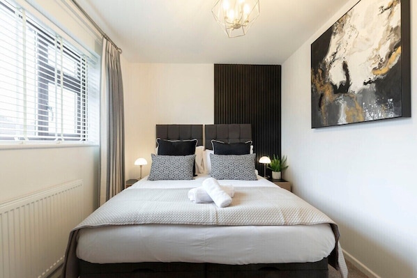 Habitación de hotel con una cama, dos mesitas de noche, una planta en maceta y un cuadro abstracto grande en la pared.