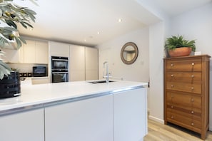Una cocina moderna con armarios blancos, horno integrado y cómoda de madera con cajones.