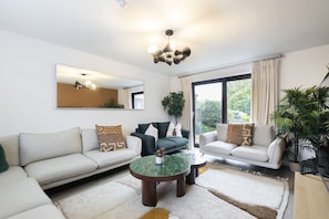 A modern living room with a large mirror, two sofas, a coffee table, and a view of greenery through the window.
