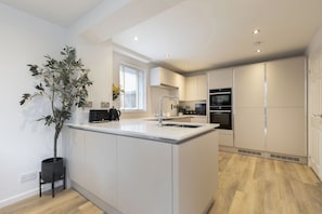 A modern kitchen with white cabinetry, a central island, a built-in oven, and a window with blinds.