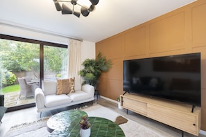 Un salón moderno con un televisor de pantalla plana grande, un sofá blanco, una mesa de centro verde y una planta en maceta.