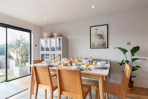 A dining area with a table set for breakfast, a cabinet with glass doors, a framed picture on the wall, and a potted plant. - Cotswold Hillside Retreat with Stunning Views (Stroud)