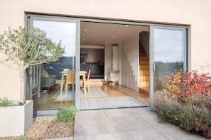 A modern house with a sliding glass door leading to a kitchen and dining area. - Cotswold Hillside Retreat with Stunning Views (Stroud)