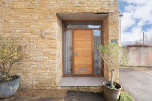 A stone building with a wooden door and a small porch. - Cotswold Hillside Retreat with Stunning Views (Stroud)