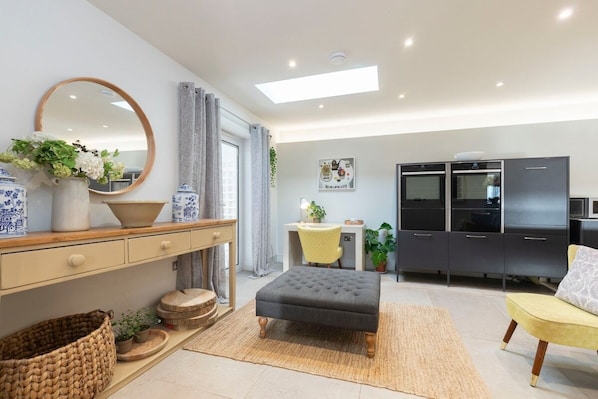 A modern living room with a sofa, ottoman, and a dining area with a table and chairs. - Cotswold Hillside Retreat with Stunning Views (Stroud)