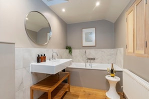 A modern bathroom with a white sink, a freestanding bathtub, and a wooden shelf. - Cotswold Hillside Retreat with Stunning Views (Stroud)