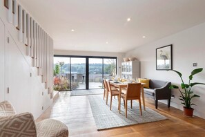 A modern living room with a dining area, a sofa, and a staircase.