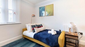 A neatly arranged bedroom with a bed, a bedside table with a lamp, and two abstract paintings on the wall. - Modern Apartment By Historic Gloucester Quays (Gloucestershire)