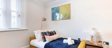 A neatly arranged bedroom with a bed, a bedside table with a lamp, and two abstract paintings on the wall.