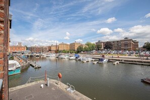 A marina with boats docked, a pedestrian walkway, and buildings in the background.