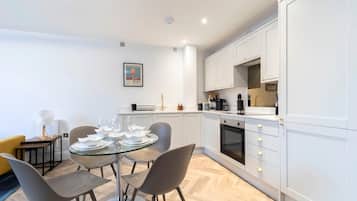 A modern kitchen with white cabinets, a dining table with chairs, and a coffee machine.