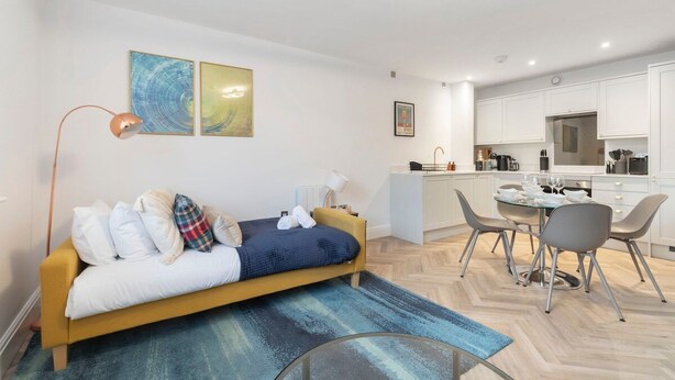 A modern apartment with a sofa, a dining table, and a kitchen area. - Modern Apartment By Historic Gloucester Quays (Gloucestershire)