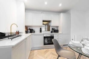 Una cocina moderna con armarios blancos, encimera negra y una mesa de comedor de vidrio.