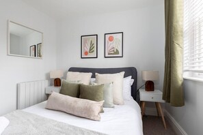 A bedroom with a bed, bedside tables, a mirror, and artwork on the wall.