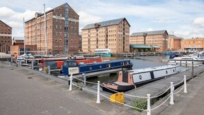 A canal-side area with moored boats, a warehouse building, and adjacent residential or commercial buildings. - Modern Apartment By Historic Gloucester Quays (Gloucestershire)