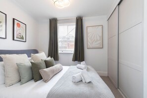 Un dormitorio ordenado con cama, almohadas, una ventana con cortinas y decoración en la pared.