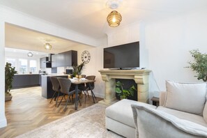 Ein modernes Wohnzimmer mit Kamin, einem Essbereich mit Stühlen und einer dahinterliegenden Küche.