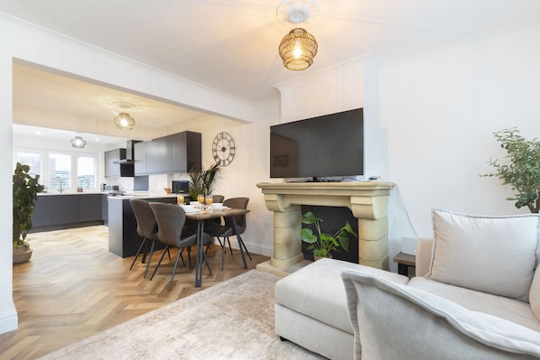 A modern living room with a fireplace, a dining area with chairs, and a kitchen in the background.