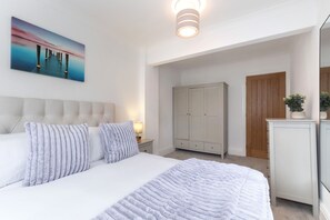 A bedroom with a large bed, a nightstand, a wardrobe, and a door leading to another room.