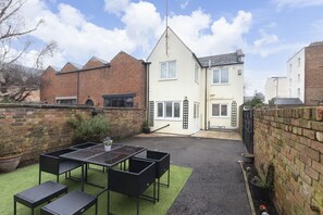 A courtyard with a table and chairs, a brick wall, and a white building with a pitched roof. - Peaceful 3-Bed Home in Tivoli (Gloucestershire)
