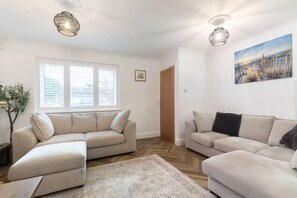 A living room with two beige sofas, a wooden herringbone floor, and a painting on the wall.