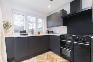 A modern kitchen with dark cabinets, a black stove, and a herringbone wood floor.