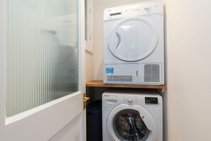 A laundry room with two stacked washing machines and a small shelf.